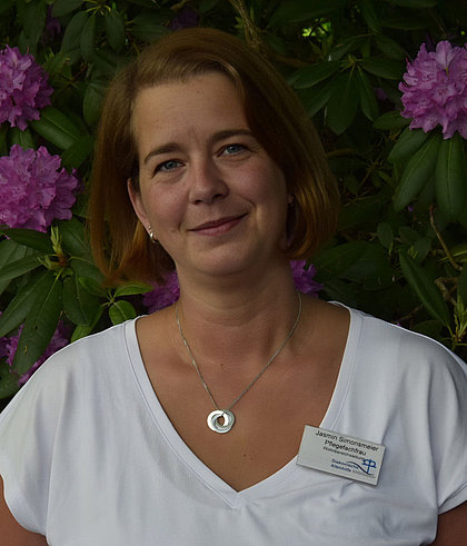Frau mit Namensschild und Kette vor lila Rhododendren