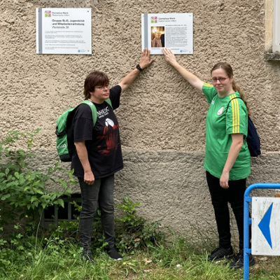 Zwei Angehörige von Volkmar Jenig berühren Gedenktafel an Hauswand